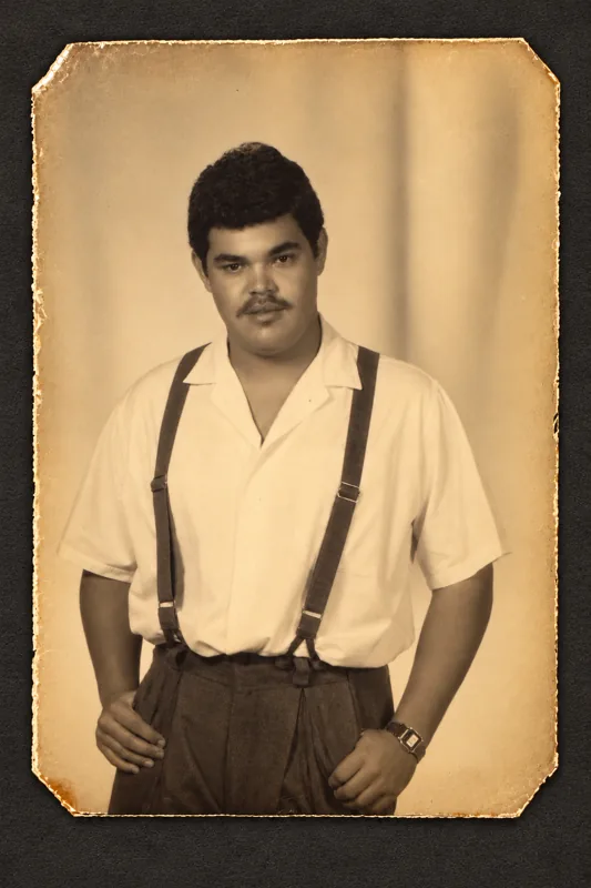 Wilfredo Pi&ntilde;eiro as a young man, in a white shirt and suspenders, in a sepia studio portrait from 1988