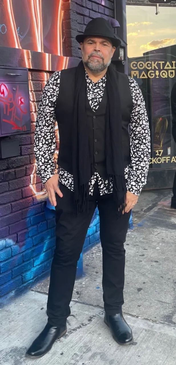 Wilfredo in a black hat and scarf on a mural-painted street