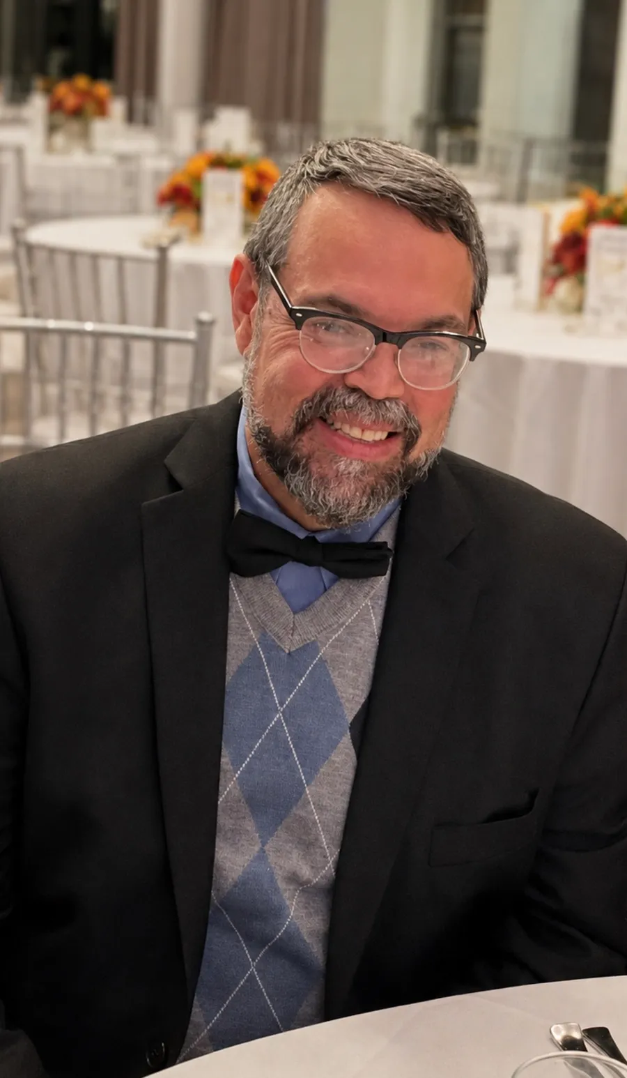 Wilfredo seated at a banquet table in a bow tie and argyle sweater