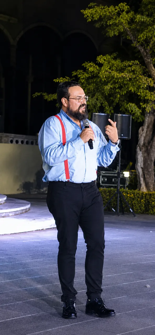 Wilfredo speaking with a microphone on an outdoor stage in the evening