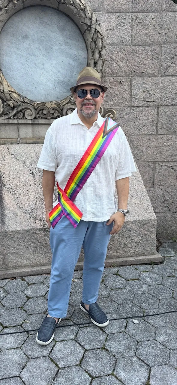 Wilfredo wearing a Progress Pride sash at an outdoor Pride event